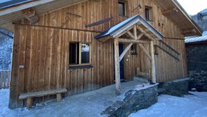 A wooden building with a sloped roof, a wooden porch, and a stone wall adjacent to it. - Chalet telegraph 13/15 people (Saint-Martin-D'arc)