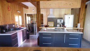 A modern kitchen with wooden cabinetry, a central island, and a view into the dining area. - Chalet telegraph 13/15 people (Saint-Martin-D'arc)
