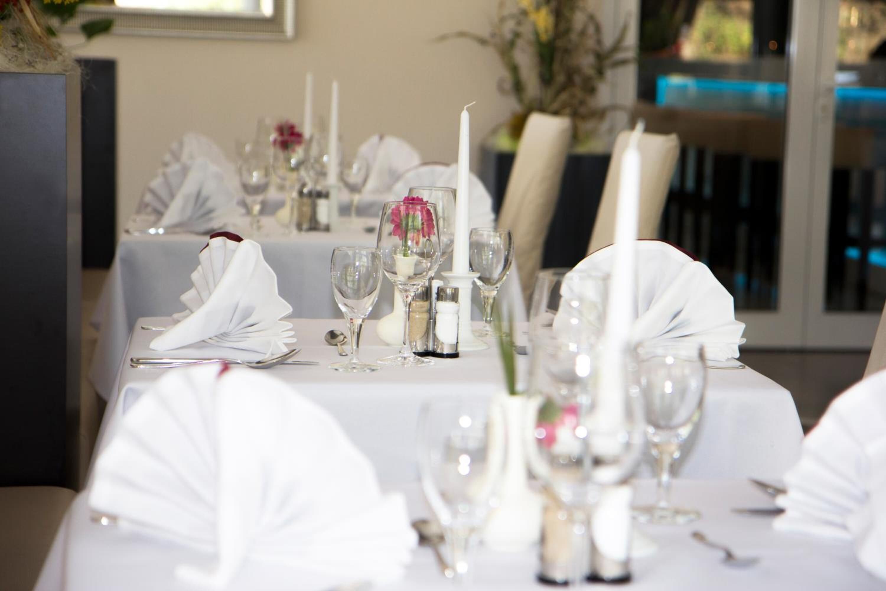 A dining table set with white tablecloths, glassware, and candles.