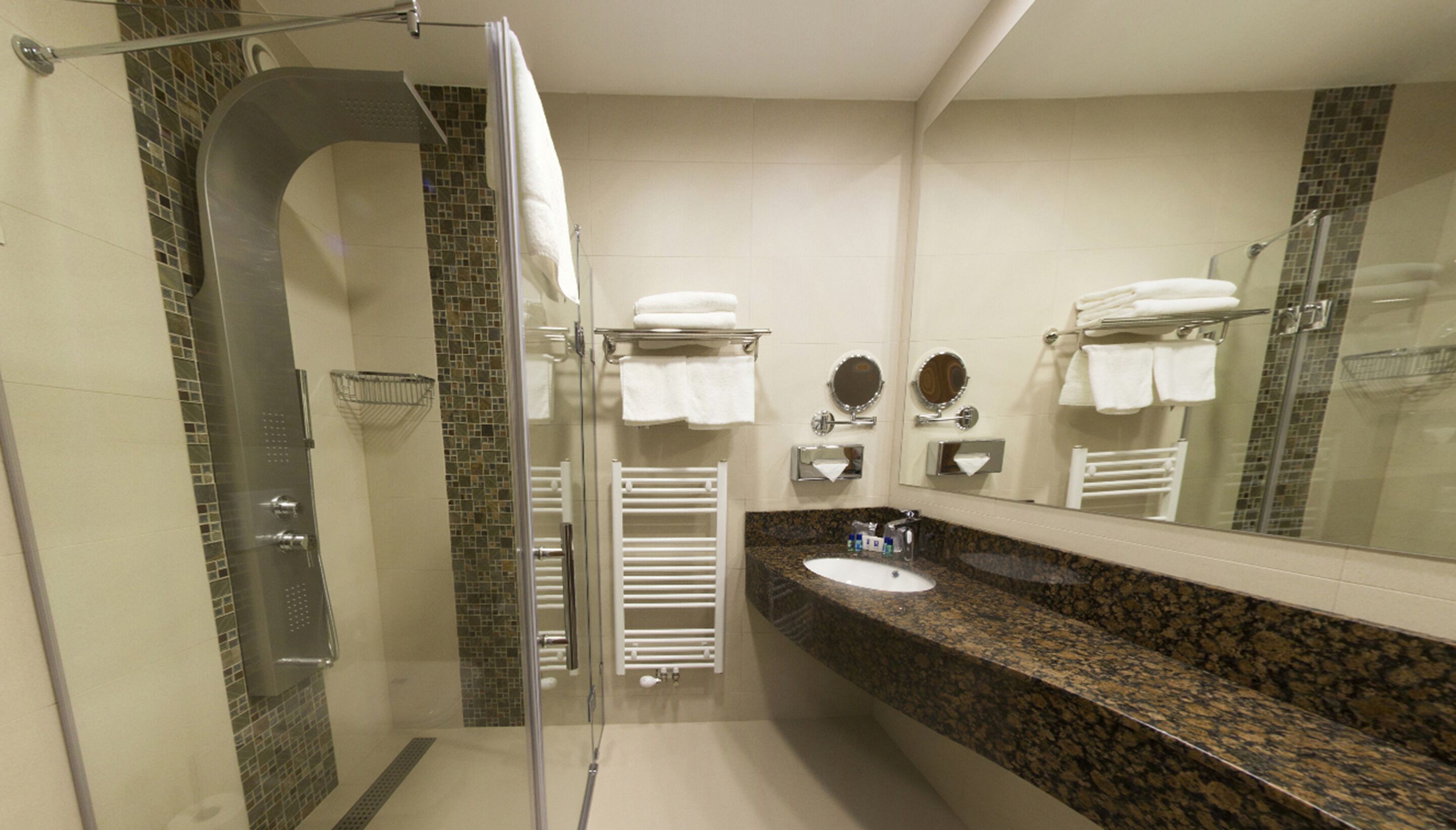 Un baño moderno con cabina de ducha de vidrio, lavabo con encimera de granito y un espejo grande.