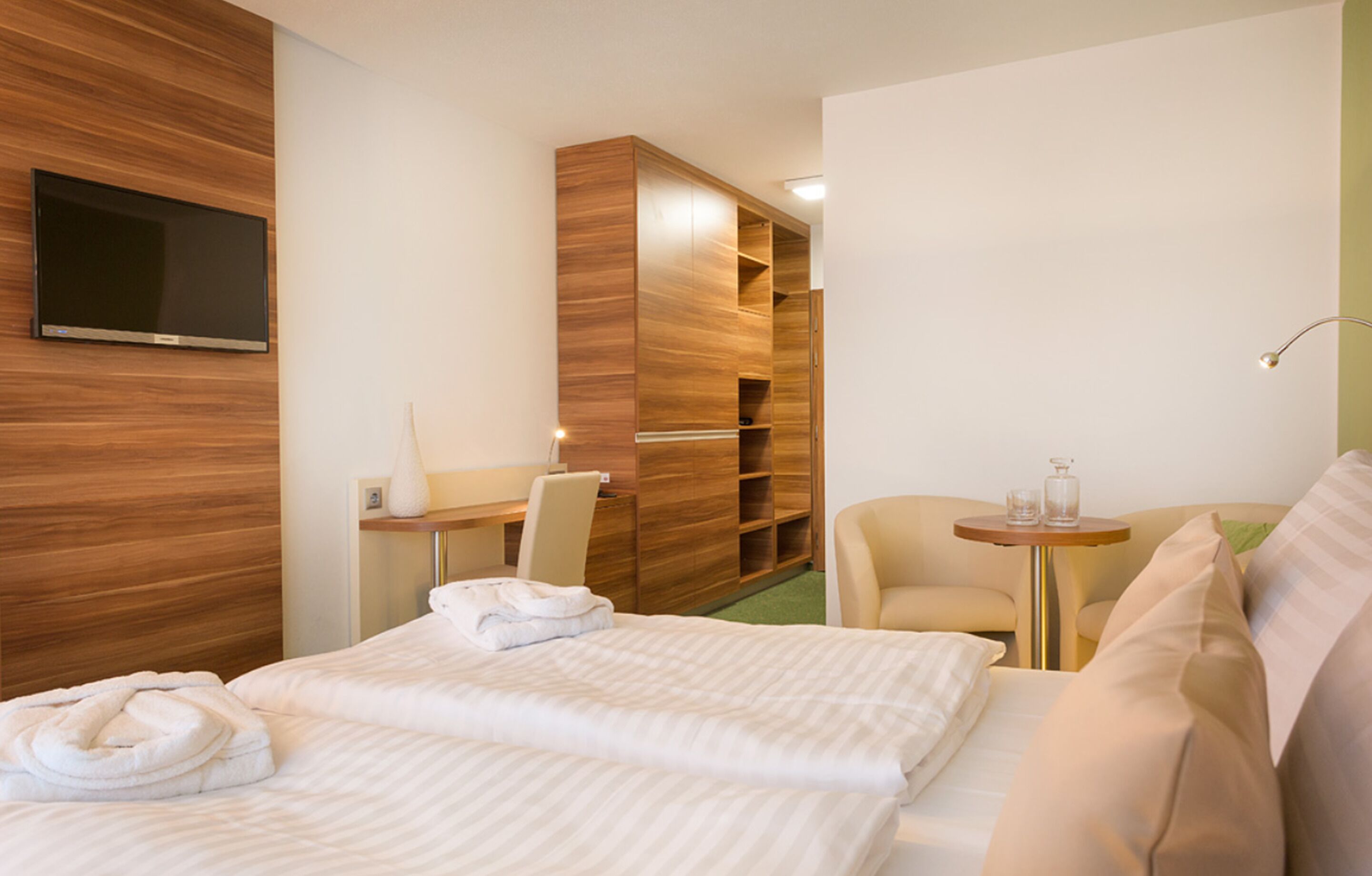 Ein Hotelzimmer mit einem Bett, einem Schreibtisch, einem Sessel, einem Fernseher und einem kleinen Tisch mit einer Lampe.