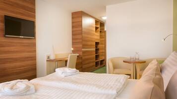 Ein Hotelzimmer mit einem Bett, einem Schreibtisch, einem Sessel, einem Fernseher und einem kleinen Tisch mit einer Lampe.
