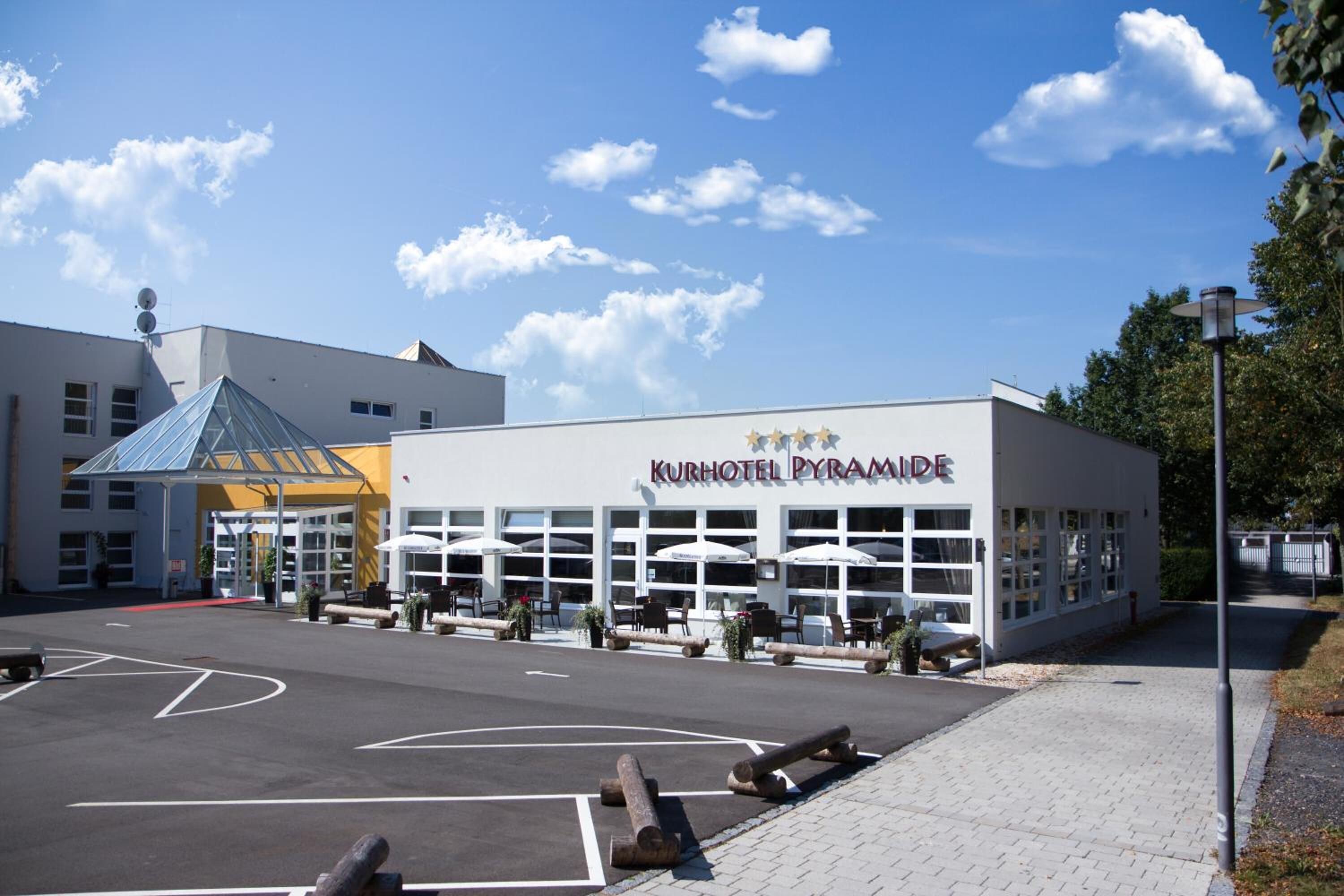 A hotel named "Kurhotel Pyramide" with a modern design, large windows, and outdoor seating areas.