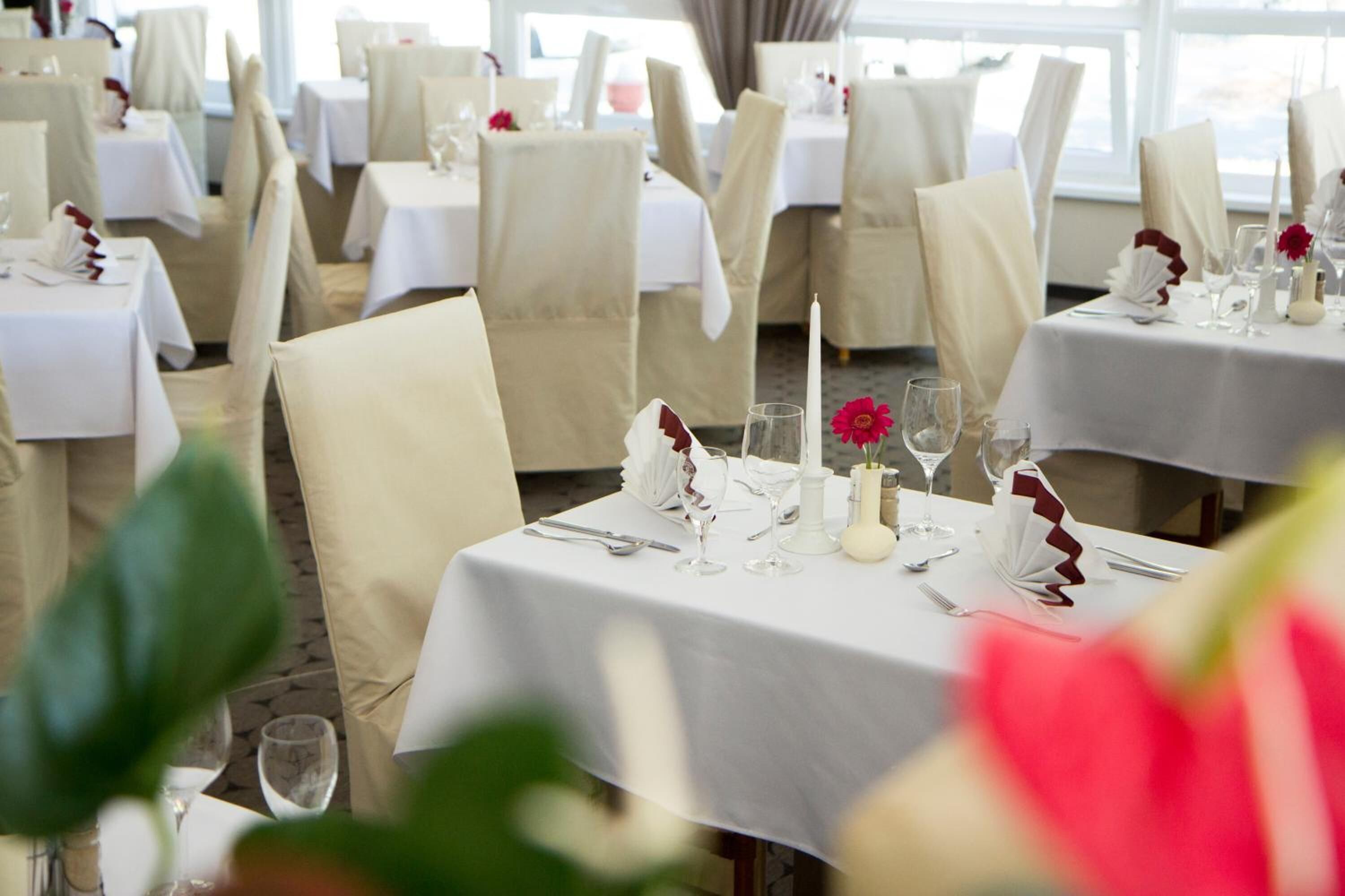 A restaurant with multiple tables set for dining, each with white tablecloths and neatly arranged cutlery.