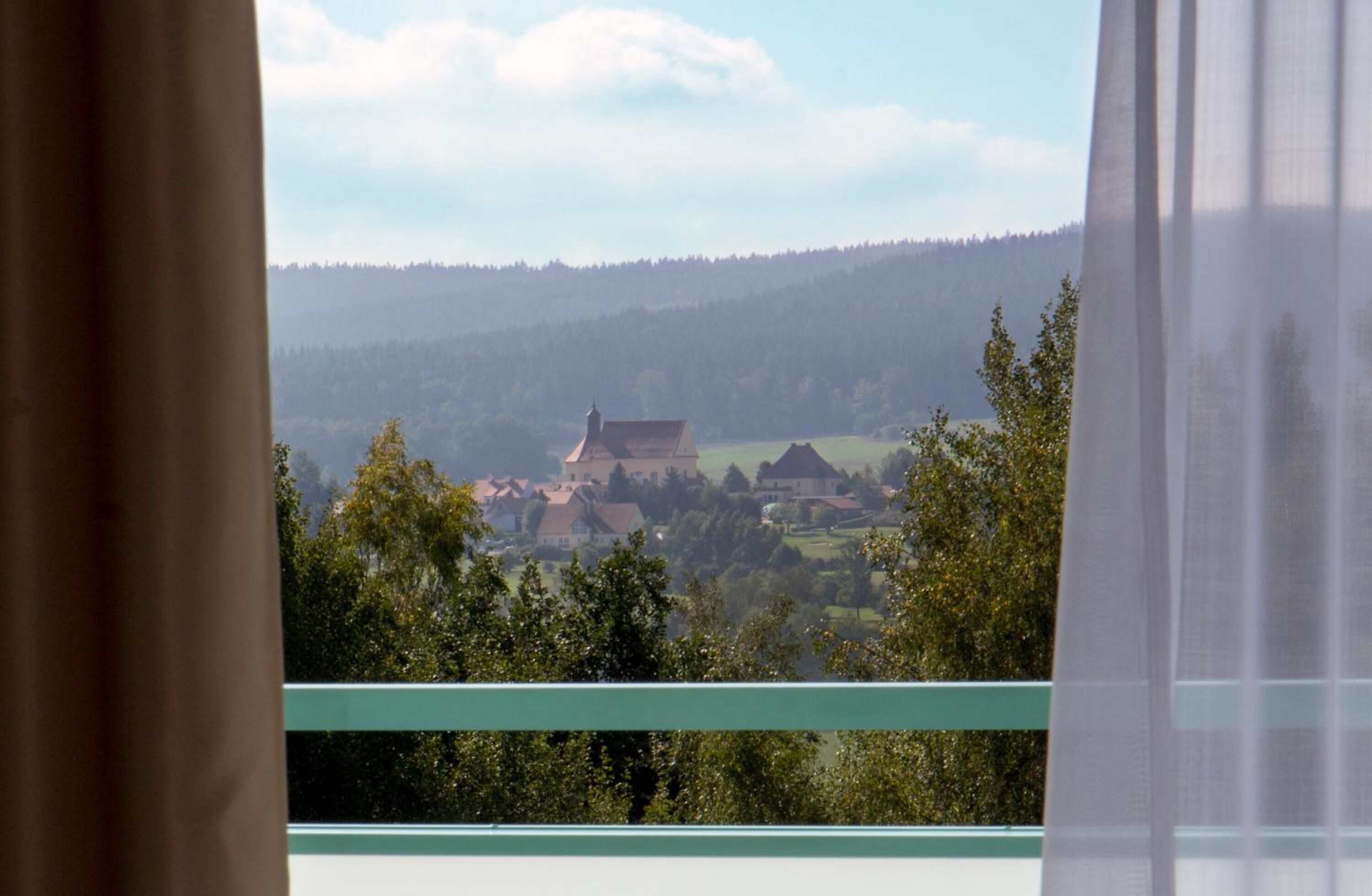 A view from a window overlooking a rural landscape with a prominent building and trees.