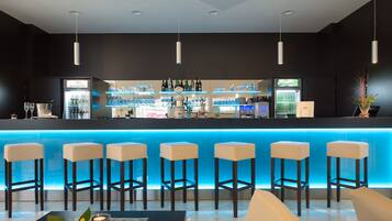 Eine moderne Bar mit einer blauen beleuchteten Theke, mehreren Barhocker und einer Auswahl an Flaschen und Gläsern.