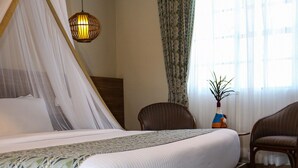 Uma cama bem arrumada com estrutura de madeira e colchão branco, luminária pendente e uma cadeira com assento de fibra.