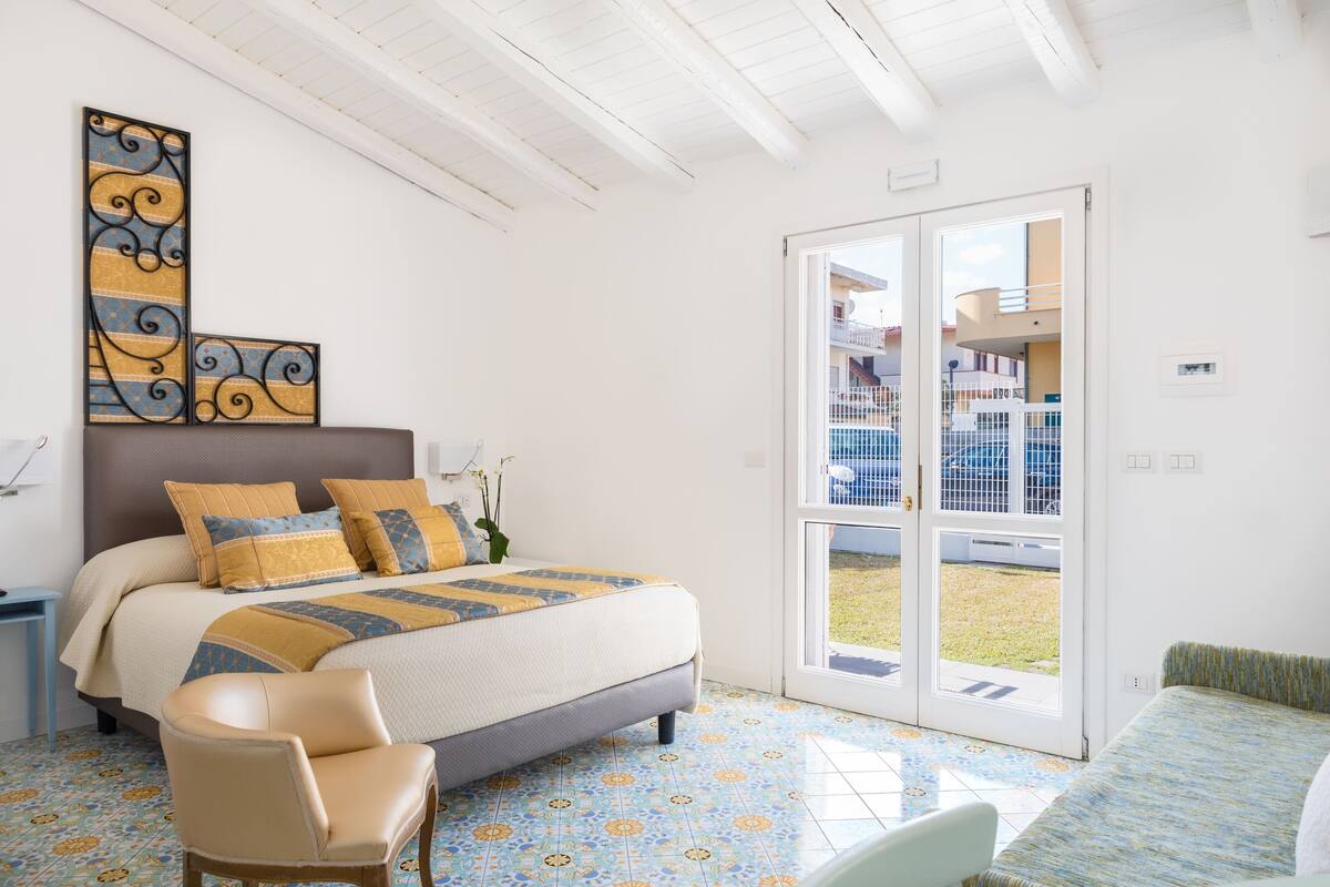 A bedroom with a bed, a chair, a large window, and a view of a pool.