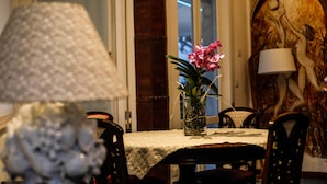 A dining table with a lace tablecloth, a vase with pink flowers, and a lamp. - La Foresteria di Maestina (Barcellona Pozzo di Gotto)