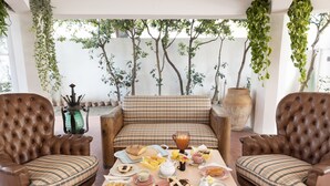 A cozy outdoor seating area with two brown leather armchairs and a plaid sofa, surrounded by potted plants and a large vase. - La Foresteria di Maestina (Barcellona Pozzo di Gotto)