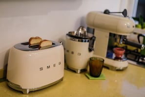 A kitchen with a white toaster, a coffee maker, and a glass of iced coffee on a countertop. - La Foresteria di Maestina (Barcellona Pozzo di Gotto)
