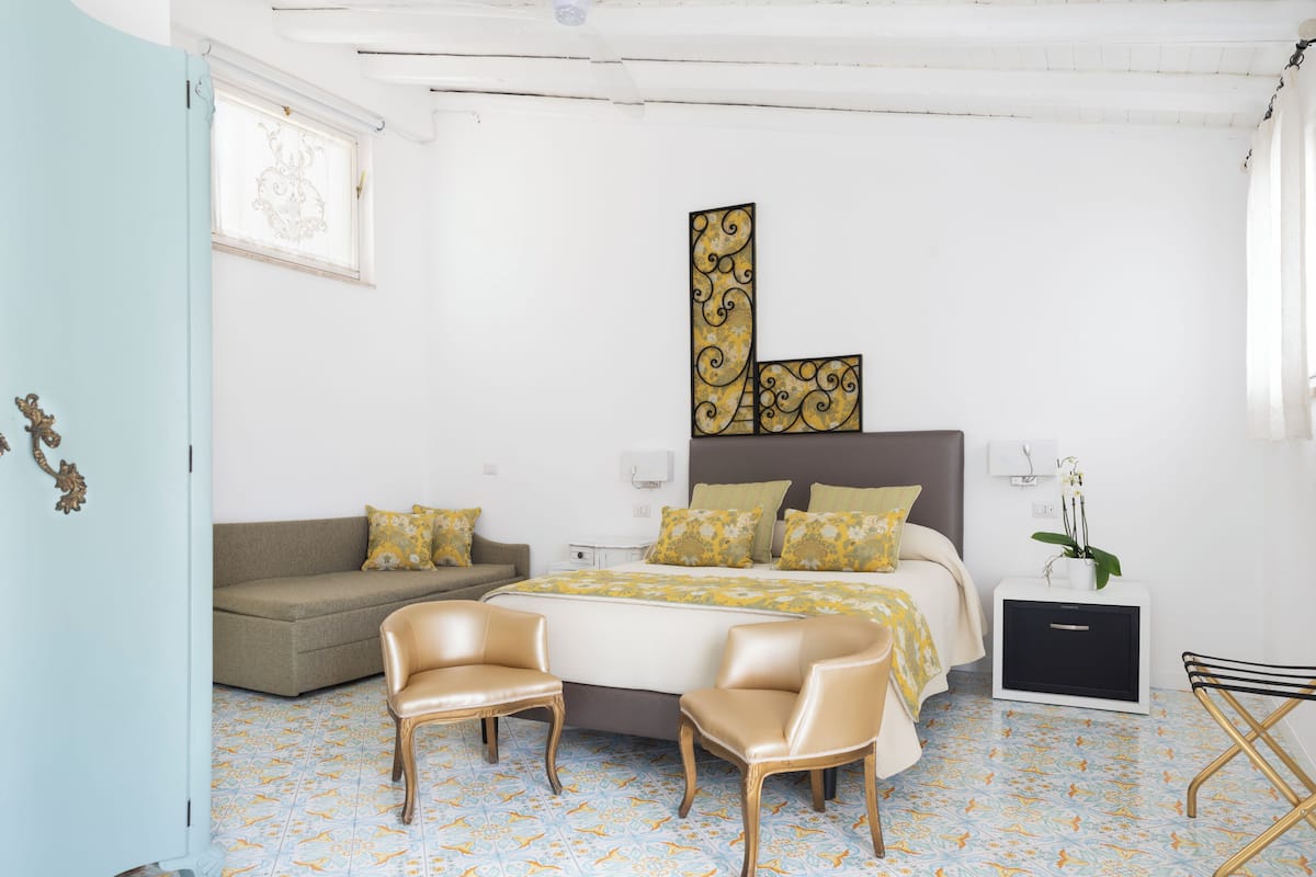 A bedroom with a bed, two chairs, a sofa, a bedside table, and a nightstand.