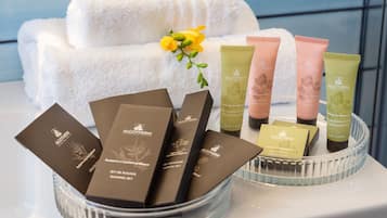 Esposizione di prodotti ALGOTHERM, tra cui crema corpo, kit da barba e shampoo, disposti su un vassoio con un asciugamano e fiori sullo sfondo.