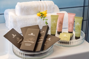 A display of ALGOTHERM products including body cream, shaving set, and shampoo, arranged on a tray with a towel and flowers in the background. - La Foresteria di Maestina (Barcellona Pozzo di Gotto)