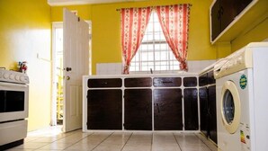 A kitchen with a washing machine, a stove, and a window with curtains.
