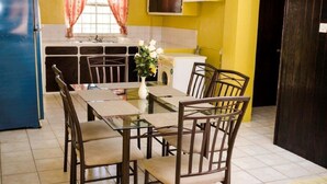 A compact kitchen with a dining area, featuring a refrigerator, a washing machine, and a table with chairs.