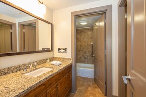 Un baño con lavamanos de encimera de granito, un espejo y zona de ducha.