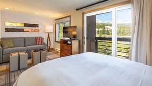 A hotel room with a large bed, a sofa, a TV, a dresser, and a balcony with a mountain view.