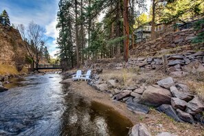 A river with a stone bridge, white chairs, and a stone wall. - Beautiful Creekside Cabin, Rooftop Hot Tub, 15min2 Red Rocks, No Pets, Licensed! (Evergreen)