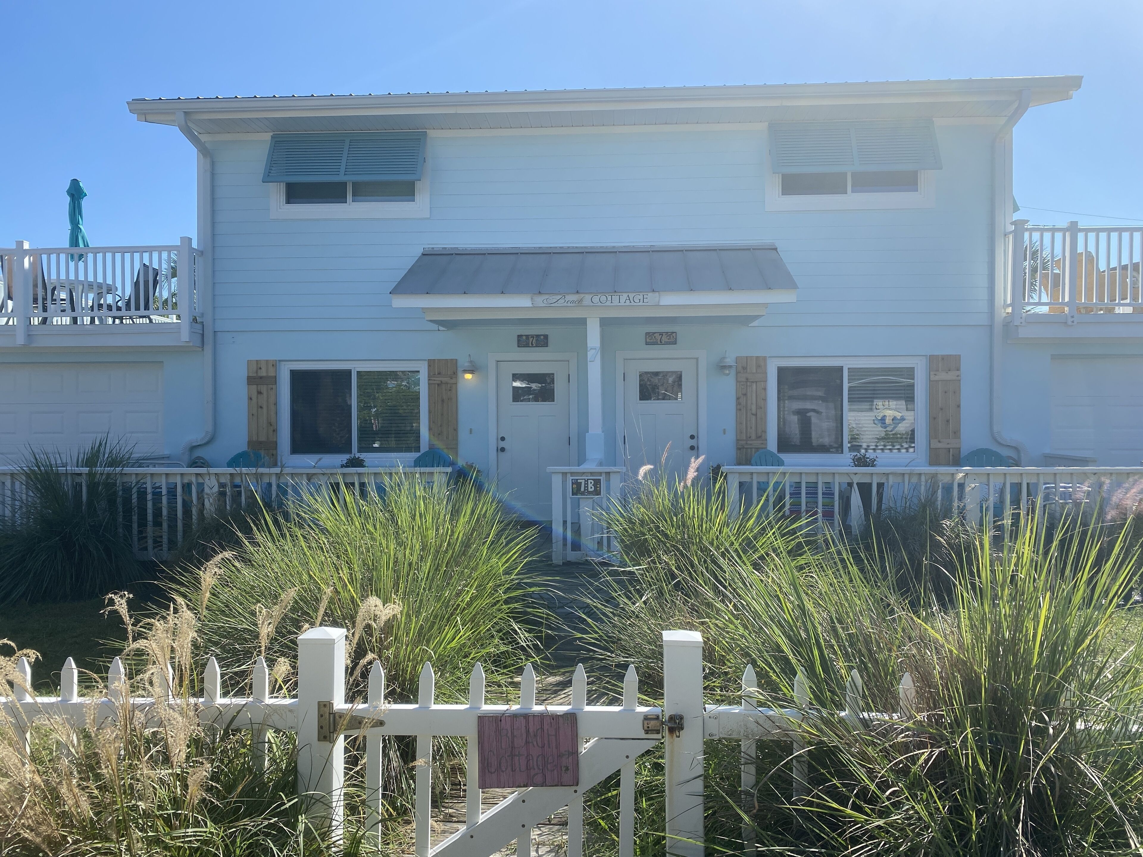 A two-story building with a porch, a sign reading "Beach Cottage," and a white picket fence.