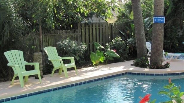 Piscina com duas cadeiras verdes e uma placa de 'Não Mergulhar'.