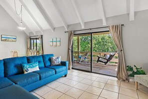 A room with a blue sofa, a dining table with chairs, a large sliding glass door leading to an outdoor patio with a rocking chair and a table. - ✨Walk 2 Beach-Pools- Golf Course Views in Seascape-2BR Memory Maker✨ (Miramar Beach)