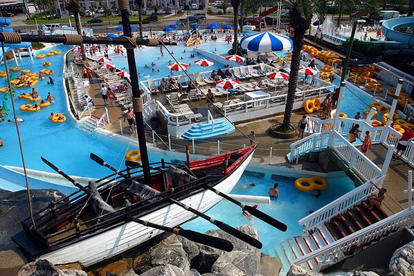 Un parque acuático interior grande con múltiples piscinas, flotadores inflables y una zona de juegos con forma de barco.