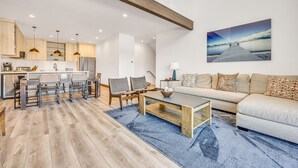 A modern living room with a sofa, coffee table, and chairs. There is a kitchen area with cabinets and a dining table. - Best Location Ski Pad in Deer Valley! Right on free shuttle route! Sleeps 16! (Deer Valley)
