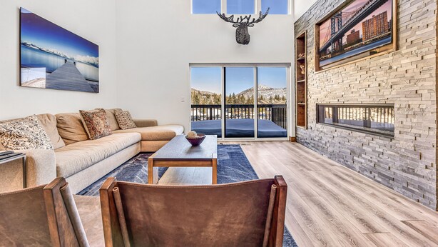 A modern living room with a sofa, coffee table, and chairs, a large painting, a deer head decoration, and a view through a glass door. - Best Location Ski Pad in Deer Valley! Right on free shuttle route! Sleeps 16! (Deer Valley)