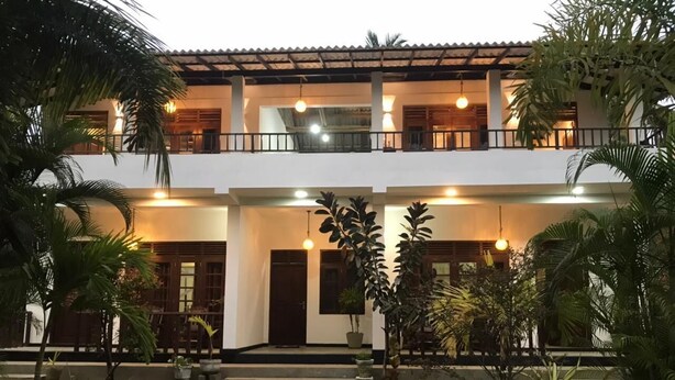 A two-story building with a symmetrical facade, a central entrance, and a small garden area with potted plants. - Sea Glow -Tangalle (Tangalle)