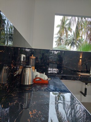 Una cocina moderna con encimera de mármol negro, electrodomésticos de acero inoxidable y vistas a palmeras a través de una ventana.