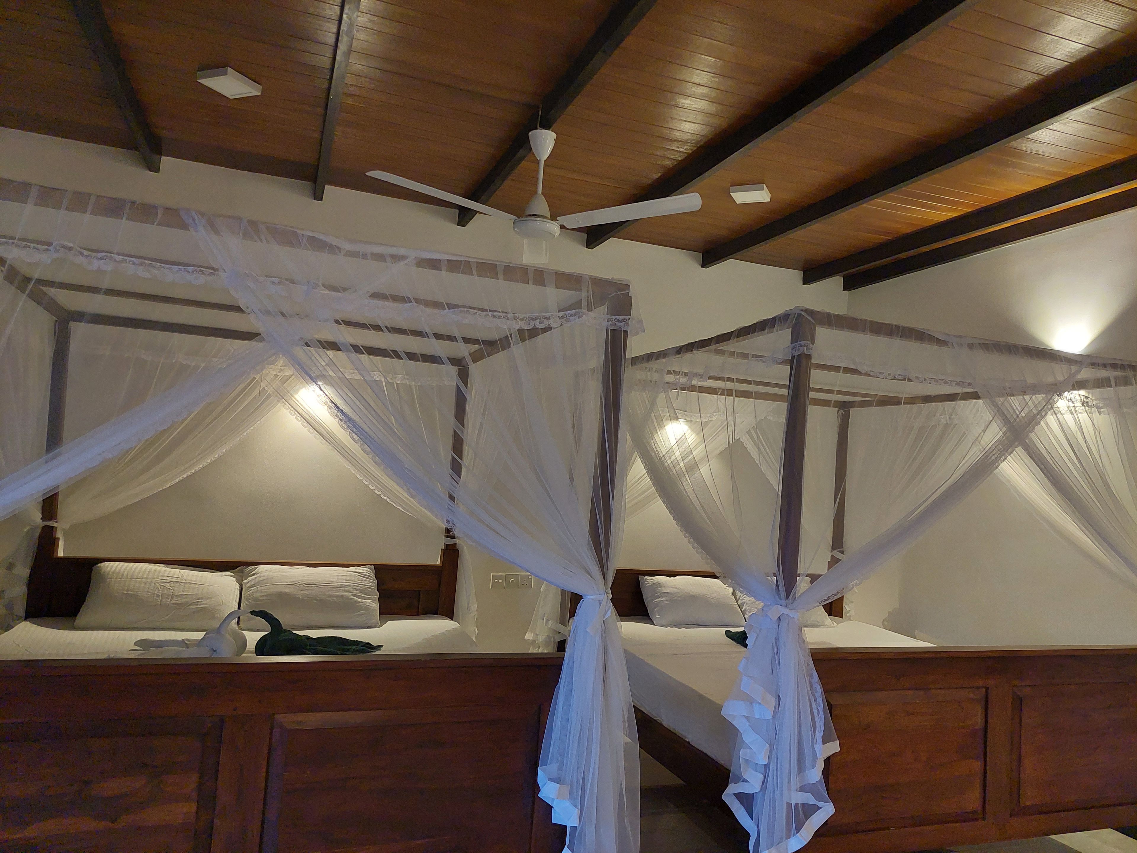 A room with two beds, each with a canopy bedspread and a ceiling fan.