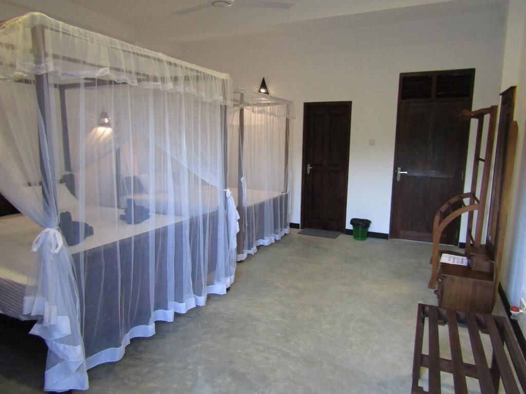 A room with two beds covered by mosquito netting, a wooden chair, and a door.