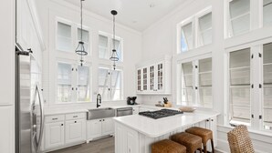 Een ruime keuken met witte kasten, een groot eiland en een eetgedeelte met rieten barstoelen.