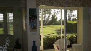 A room with a sliding glass door leading to a lawn. There are two white chairs and a potted plant. - 2 Bed 2 Bath First Floor Condo in Stoneybrook of Estero Golf Community  (Estero)
