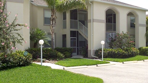 A two-story building with a central staircase, a covered entrance, and a landscaped front yard with a curved driveway. - 2 Bed 2 Bath First Floor Condo in Stoneybrook of Estero Golf Community  (Estero)