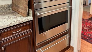 Un horno doble de acero inoxidable con pantalla digital, integrado en muebles de madera y una encimera de mármol.