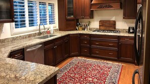 Una cocina con gabinetes de madera oscura, encimeras de granito, estufa a gas y refrigerador.