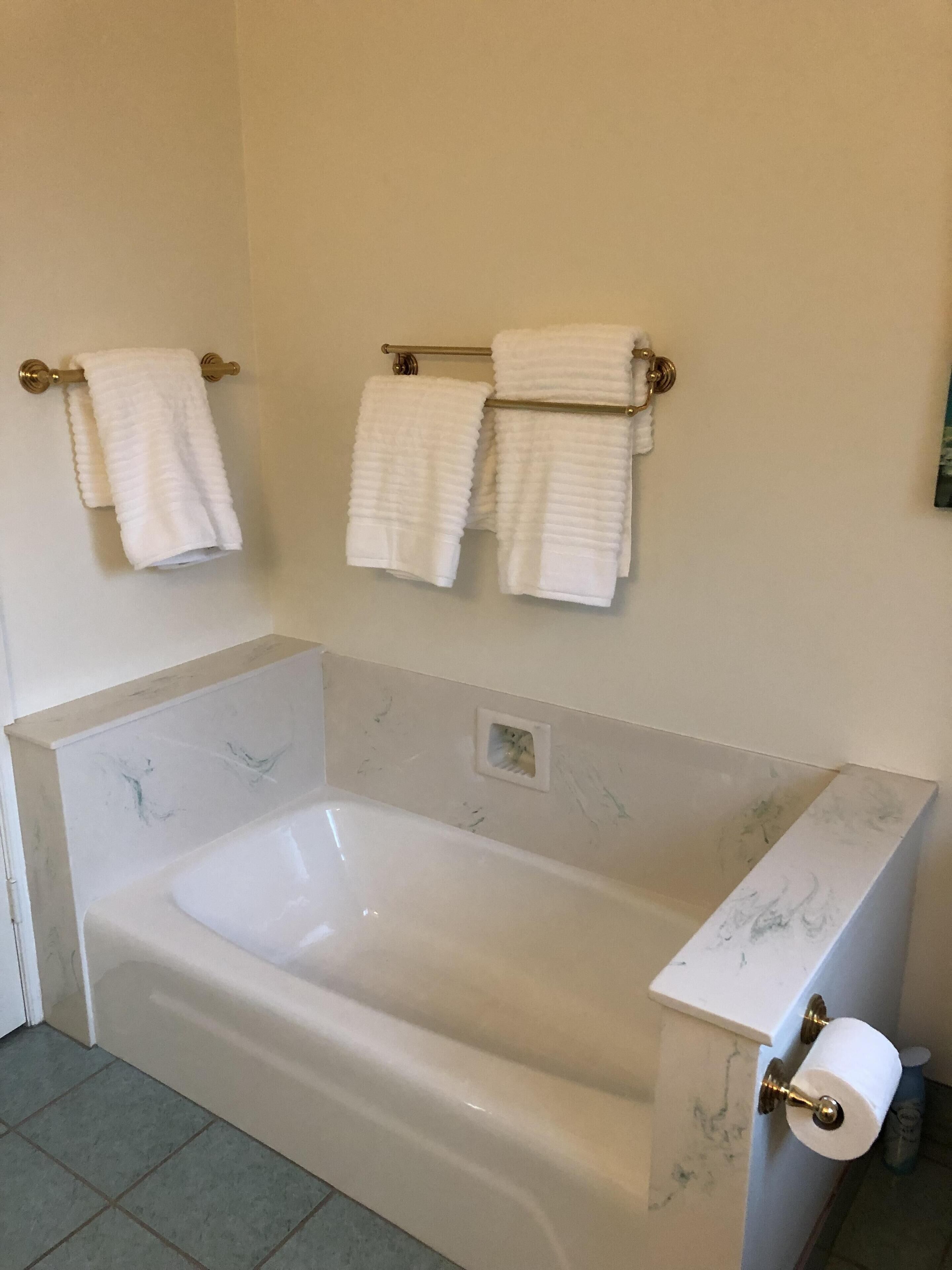 Ein Badezimmer mit einer großen Badewanne, zwei Handtuchhaltern mit weißen Handtüchern und einem Toilettenpapierhalter.