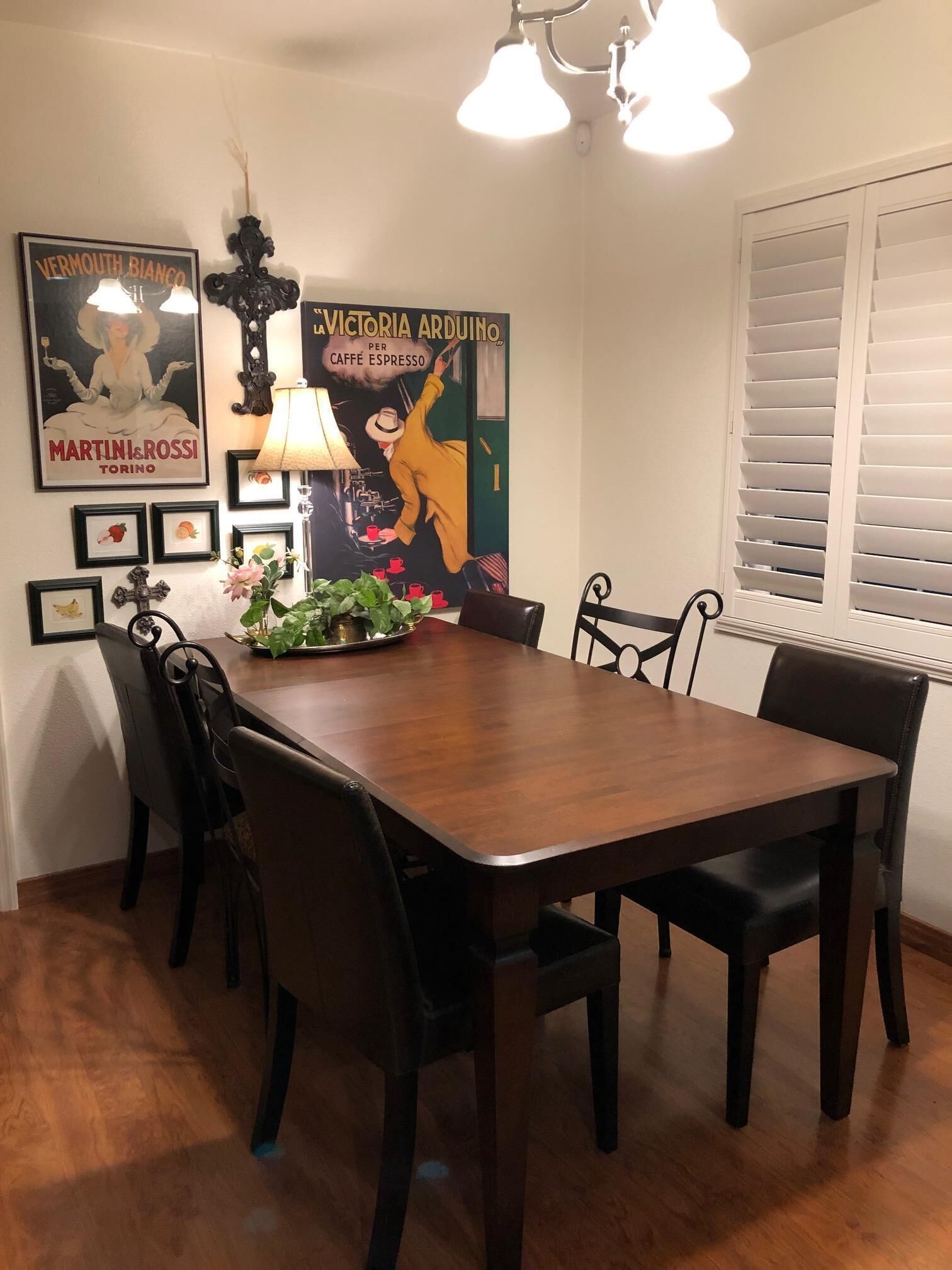 Un coin repas avec une table en bois et six chaises, une plante en pot et des éléments de décoration murale, notamment une affiche et une lampe.
