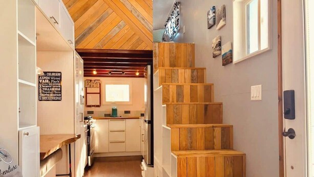 Een smalle gang die uitkomt bij een keuken met houten vloeren en een trap met houten treden.