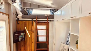 Een kleine kamer met een stapelbed, een houten trap, een bureau en een plank.