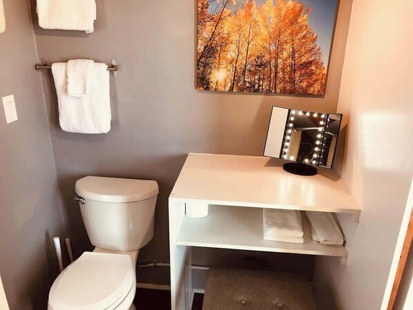 Un baño con inodoro, lavamanos con tocador, toallero y un cuadro en la pared.