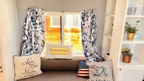 Een knus zithoekje met een comfortabele bank, decoratieve kussens en een raam met gordijnen.