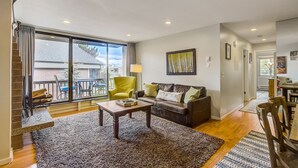 A spacious living room with a large sliding glass door leading to a balcony, a cozy sofa set, a coffee table, and a dining area with a wooden table and chairs.