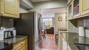 A kitchen with granite countertops, stainless steel appliances, wooden cabinets, and a view to a living area.