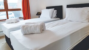 A hotel room with two beds, a window with curtains, a lamp, and a painting on the wall. - Evergreen Apartments (Northampton)