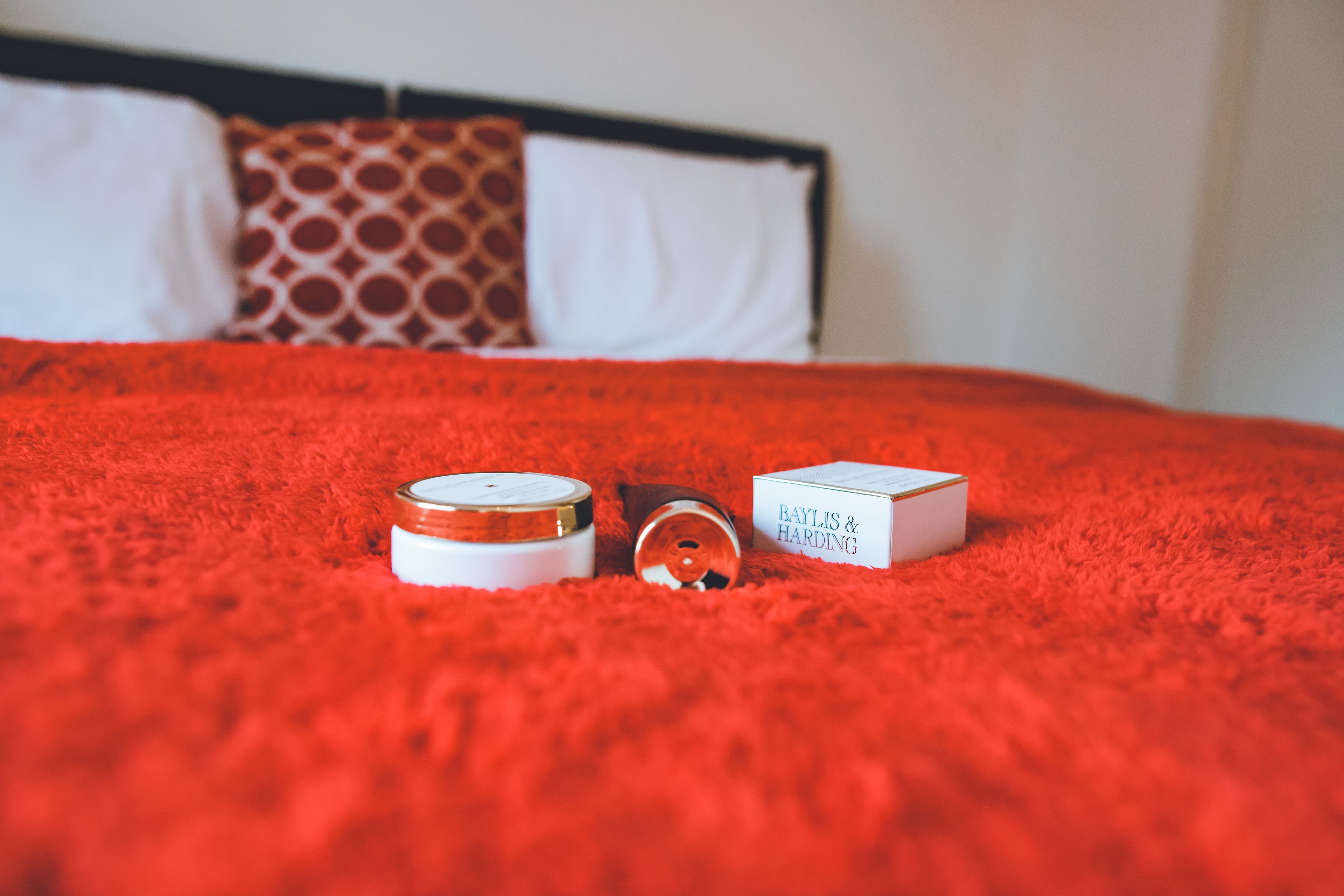 Un lit avec une couverture rouge, un oreiller blanc et un autre oreiller à motifs.