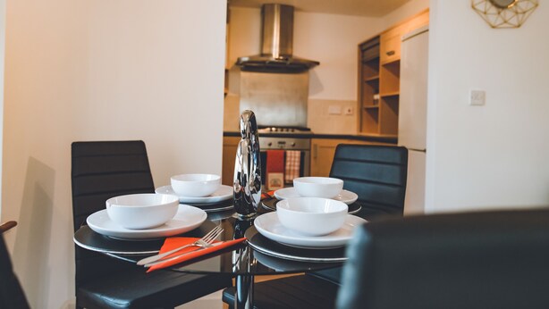A dining table set with white bowls and plates, black chairs, and a red napkin. - Evergreen Apartments (Northampton)