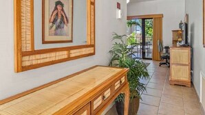 A room with a wooden desk, a framed picture on the wall, a potted plant, and a view of the outdoors. - Ocean Front Condo at The Royal Sea-Cliff Resort (Kailua Kona)